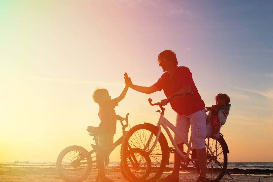 Father and kids biking on the beach at sunrise during a family wellness vacation