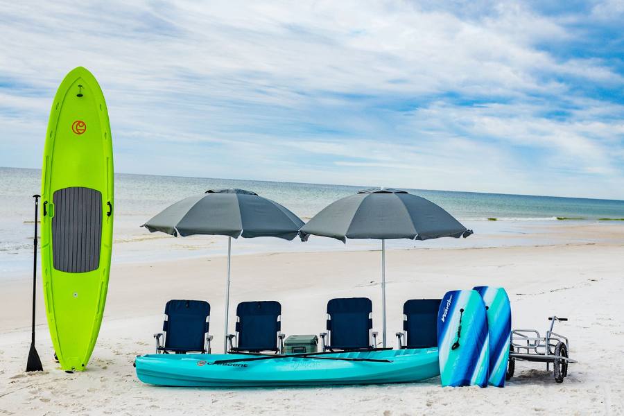 Green kayak, paddle board, and two boogie boards on a beach